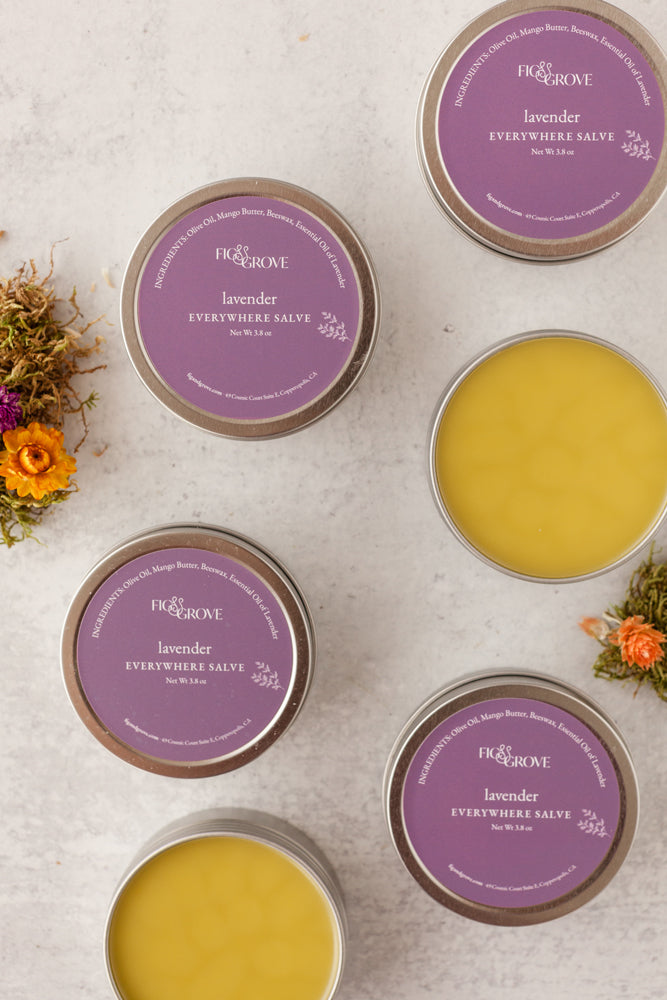 Multiple tins of Lavender 'Everywhere Salves' with purple labels on a light surface - Fig & Grove